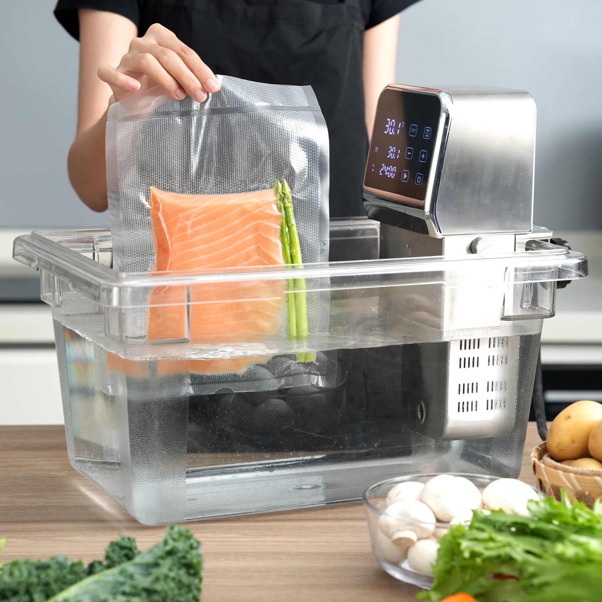 Person using a sous vide cooker with food items on a kitchen counter